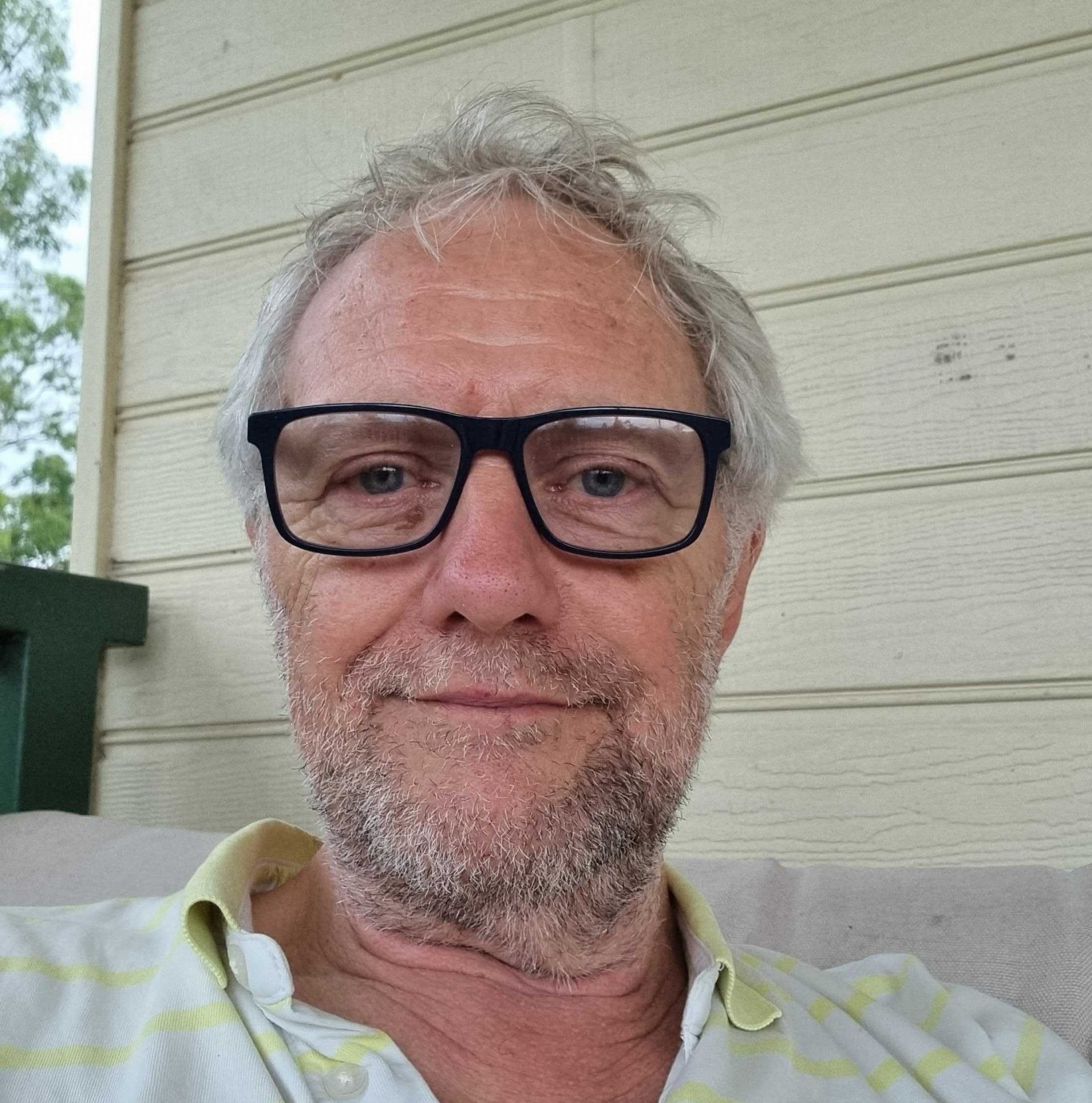 Pete smiling at the camera, wearing thick black rim glasses and a white and cream striped polo shirt